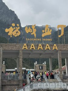 稻城亚丁景区大门，5A级景区金色标识与游客排队入园场景